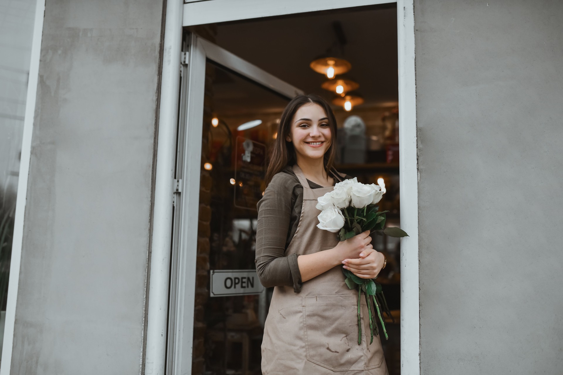 Smiling Florist Holding White Roses Outside Her Shop Entrance on a City Street